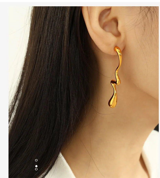 Gold earring worn by a person with dark hair and a white shirt.