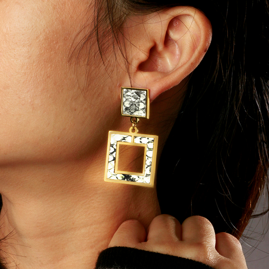 Close-up of a person wearing gold square earrings with marbled design.
