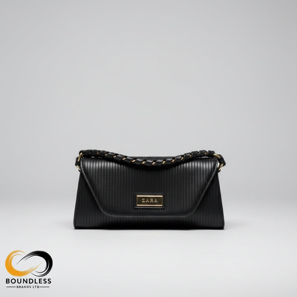 Black handbag on a wooden surface with an open book and glasses nearby, blurred background