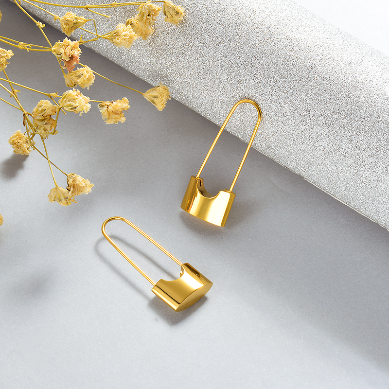 Gold safety pin earrings on a light gray surface with dried flowers.