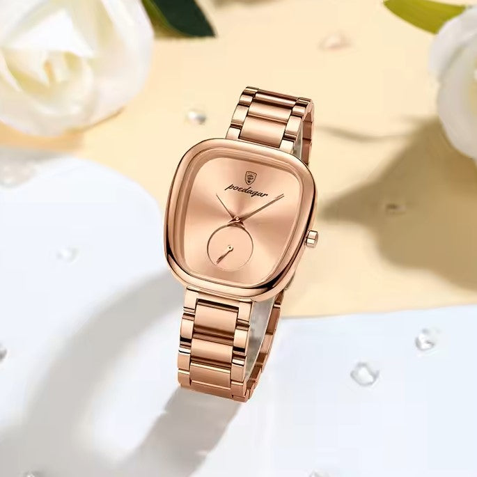 Rose gold watch on a white surface with flowers in the background