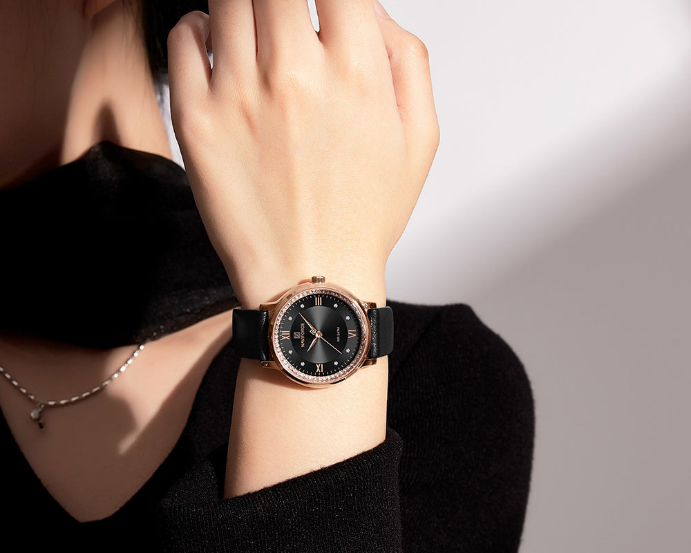 Hand wearing a black wristwatch with a rose gold case on a blurred background