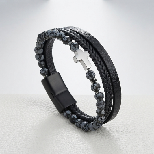 A multi-strand men's bracelet featuring a black leather band, a braided black cord, dark gray marbled beads, and a polished silver cross clasp, displayed on a light gray textured surface.