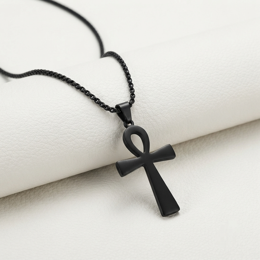 A matte black ankh cross pendant necklace on a black box chain, displayed on a textured white cylindrical prop.