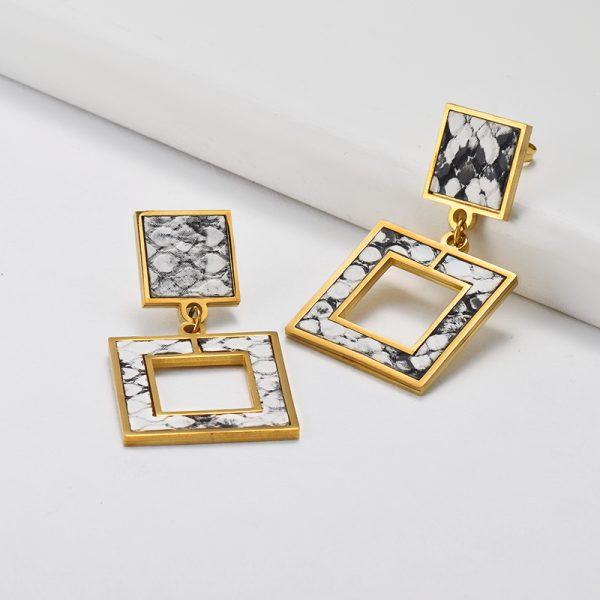 Gold and marble square earrings on a white surface