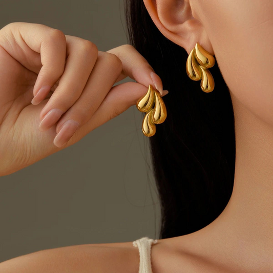 Gold earrings being worn on a model against a neutral background