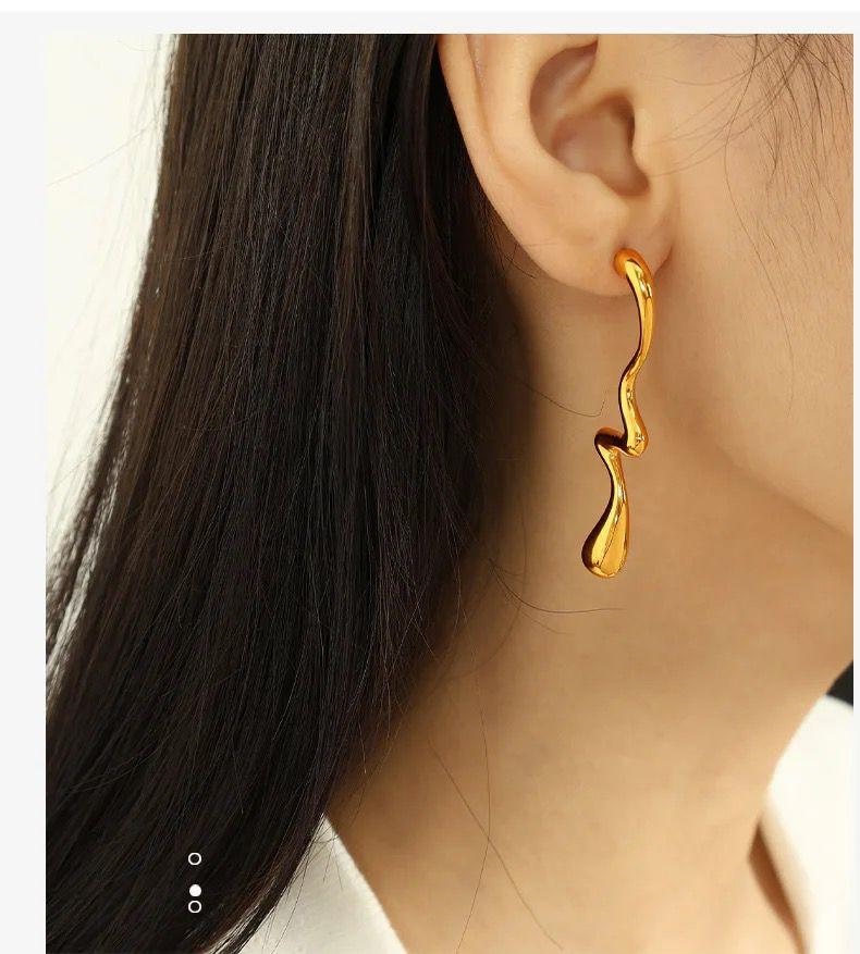 Gold earring worn by a person with dark hair and a white shirt.