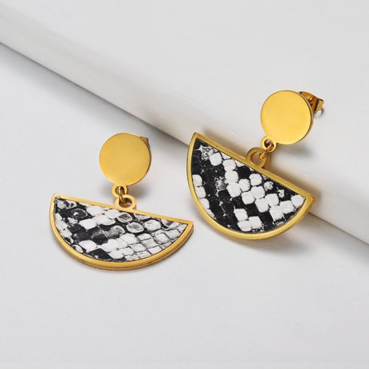 Gold and black patterned earrings on a white surface
