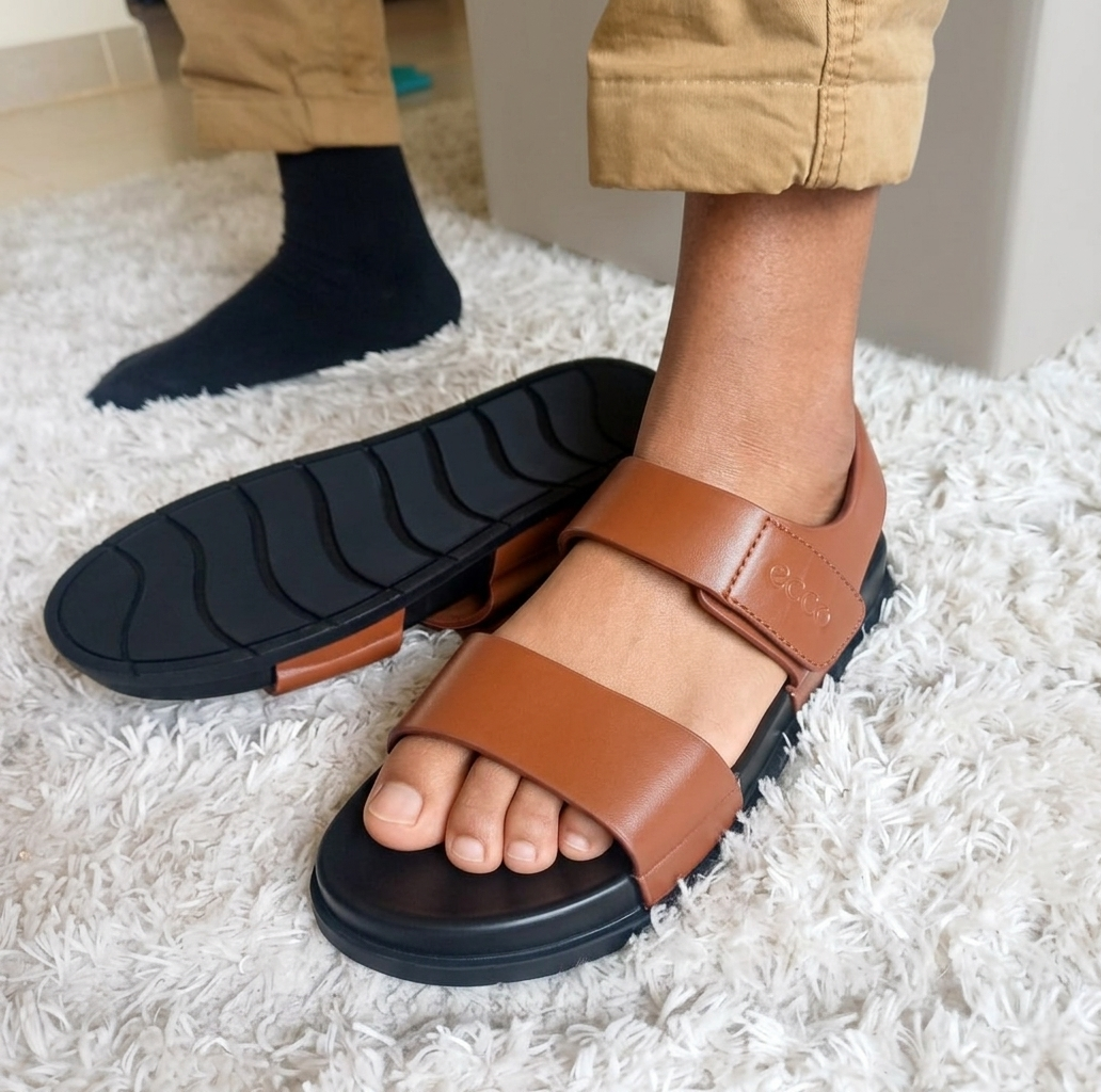 Brown sandals with black soles worn by a person on a white carpet