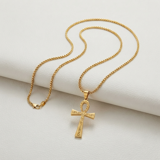 A gold chain necklace with an ankh pendant engraved with the Greek phrase 'DE OPPRESSO LIBER', displayed on a textured white surface.